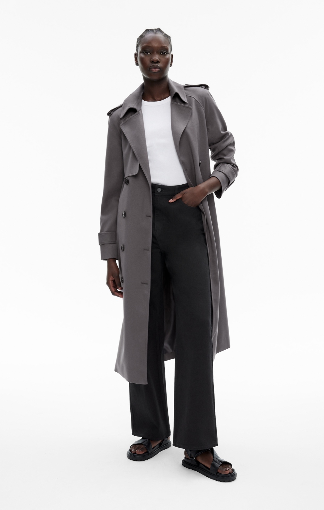 Woman in a grey trench coat, white t-shirt, black jeans and black sandals