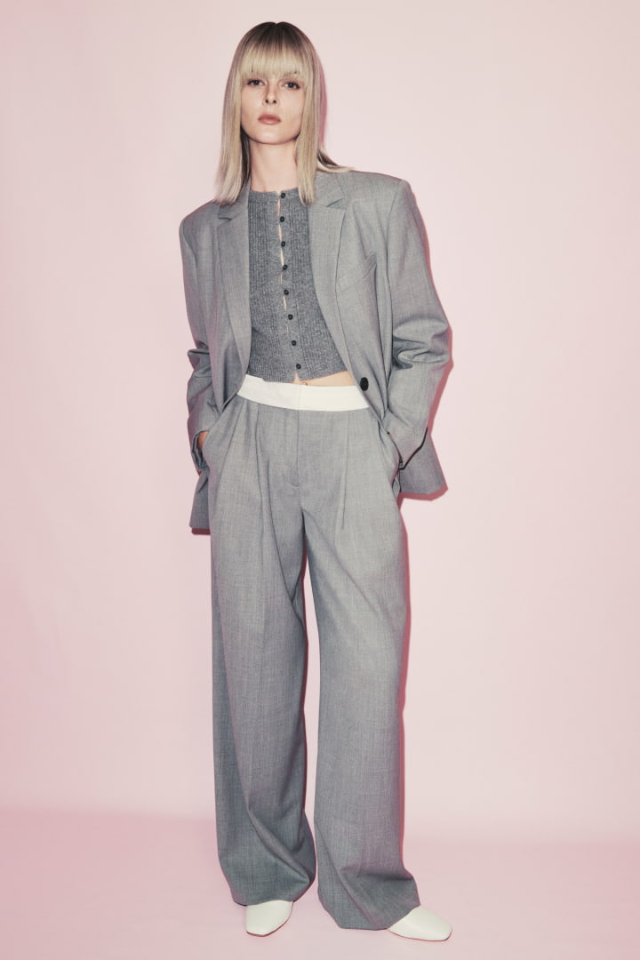 Woman in pale grey melange boxy single breasted blazer, pale grey wool blend button front knit and pale grey waist detail pant