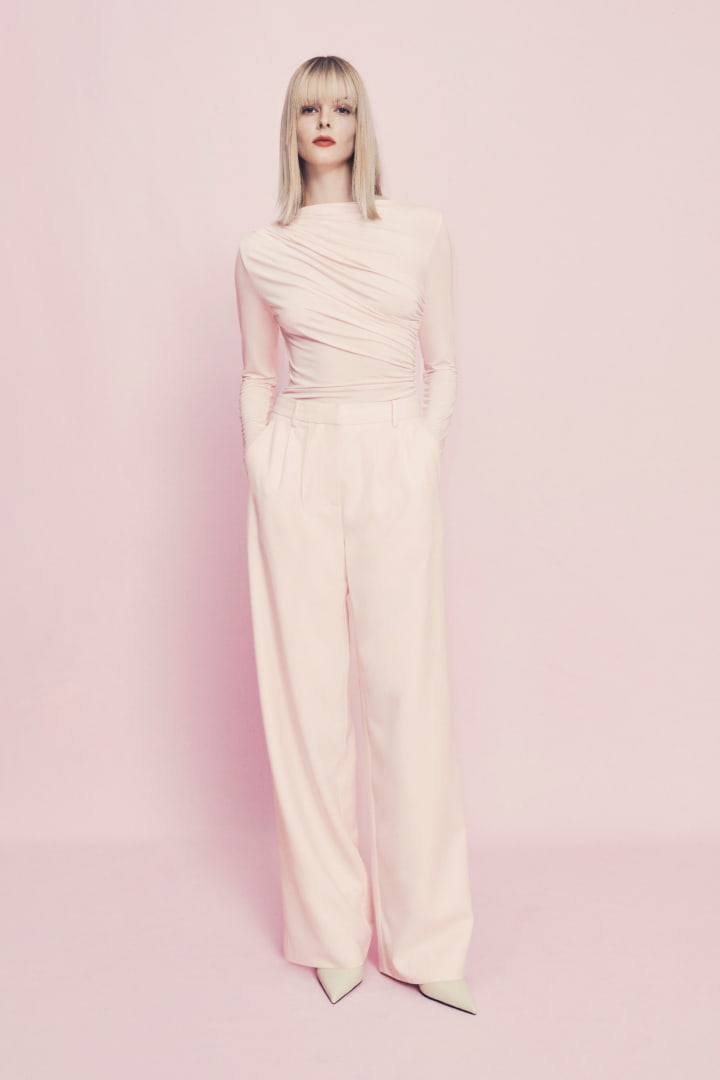 Woman in cosmetic pink jersey drape top, cosmetic pink tailored pant and stone quinn kitten mule