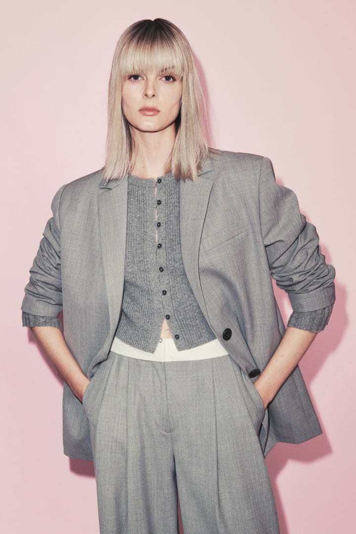 Woman in pale grey melange boxy single breasted blazer, pale grey wool blend button front knit and pale grey waist detail pant