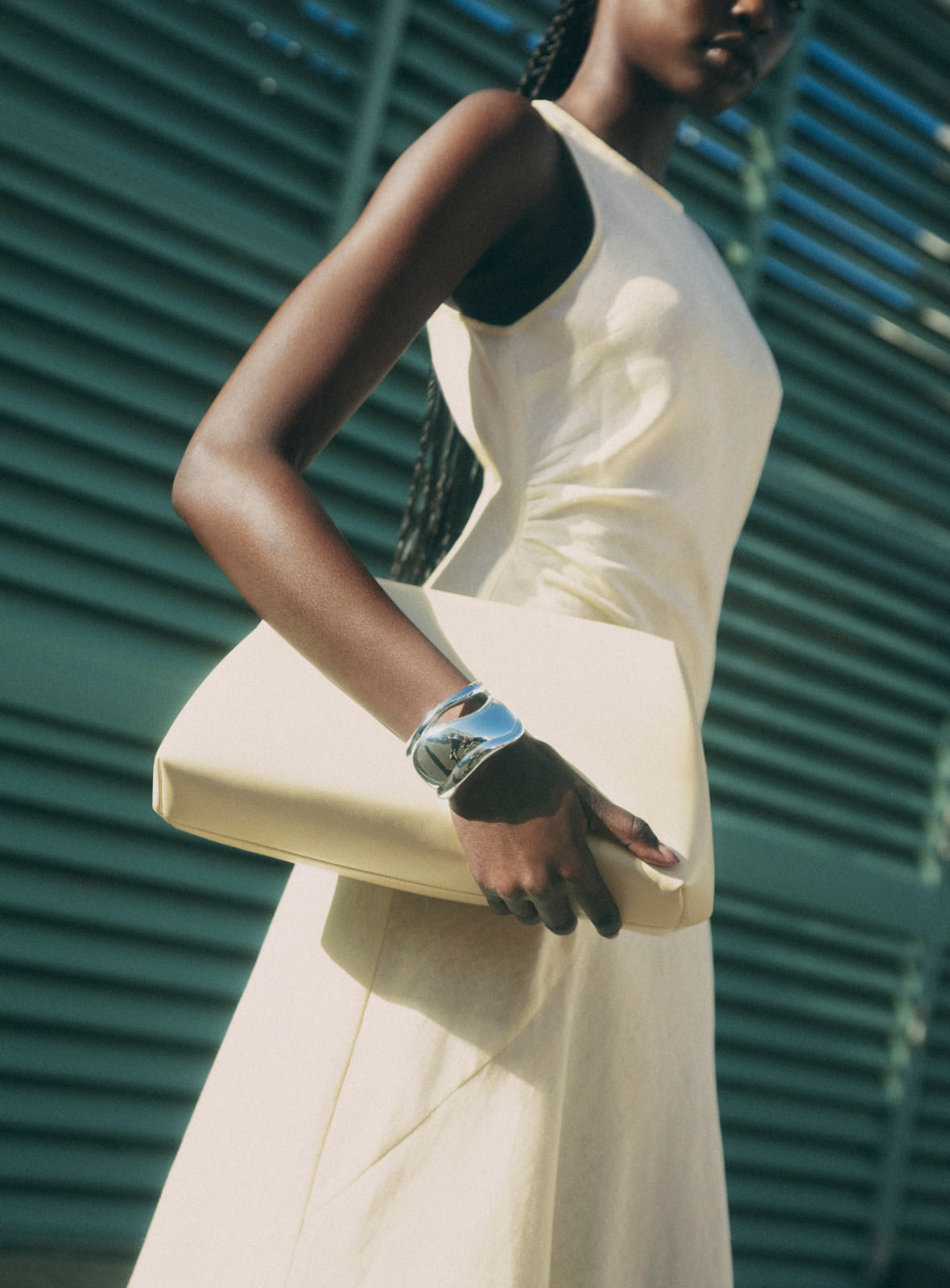 Woman wearing the lemon waist tuck detail dress, lemon ines pillow clutch, silver noa cuff and silver elora cuff wrist