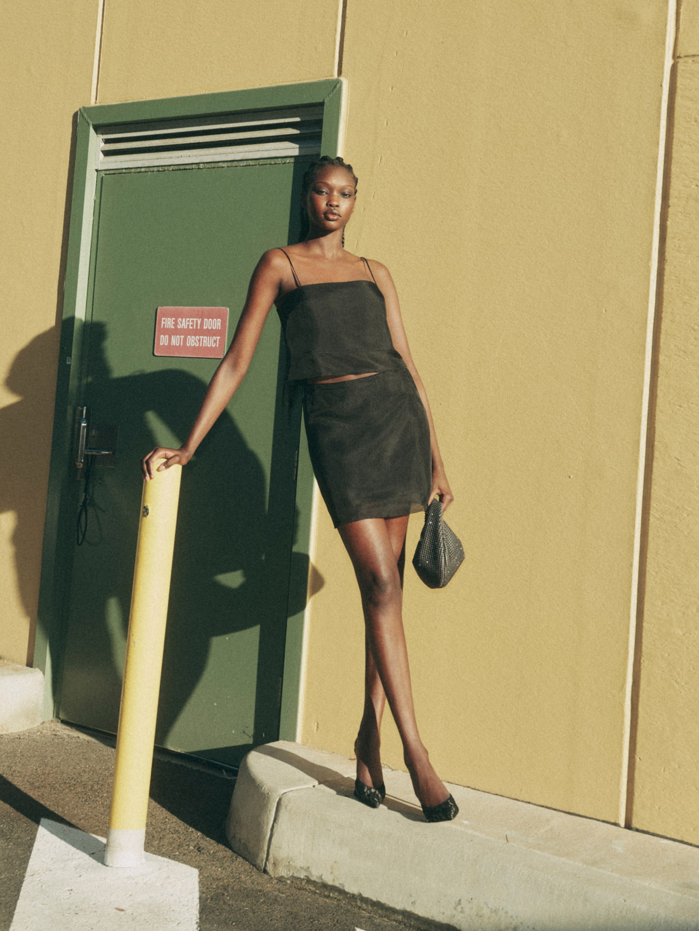 Woman wearing the black silk organza bodice, black silk organza skirt, black sasha mules and charcoal romy mini jewel bag