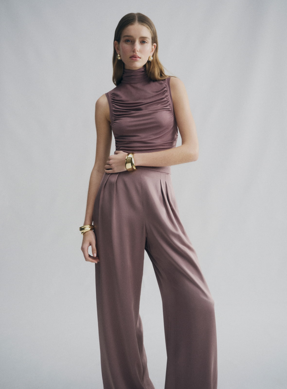 Woman in brown high neck gather top and brown pleat fluid pant